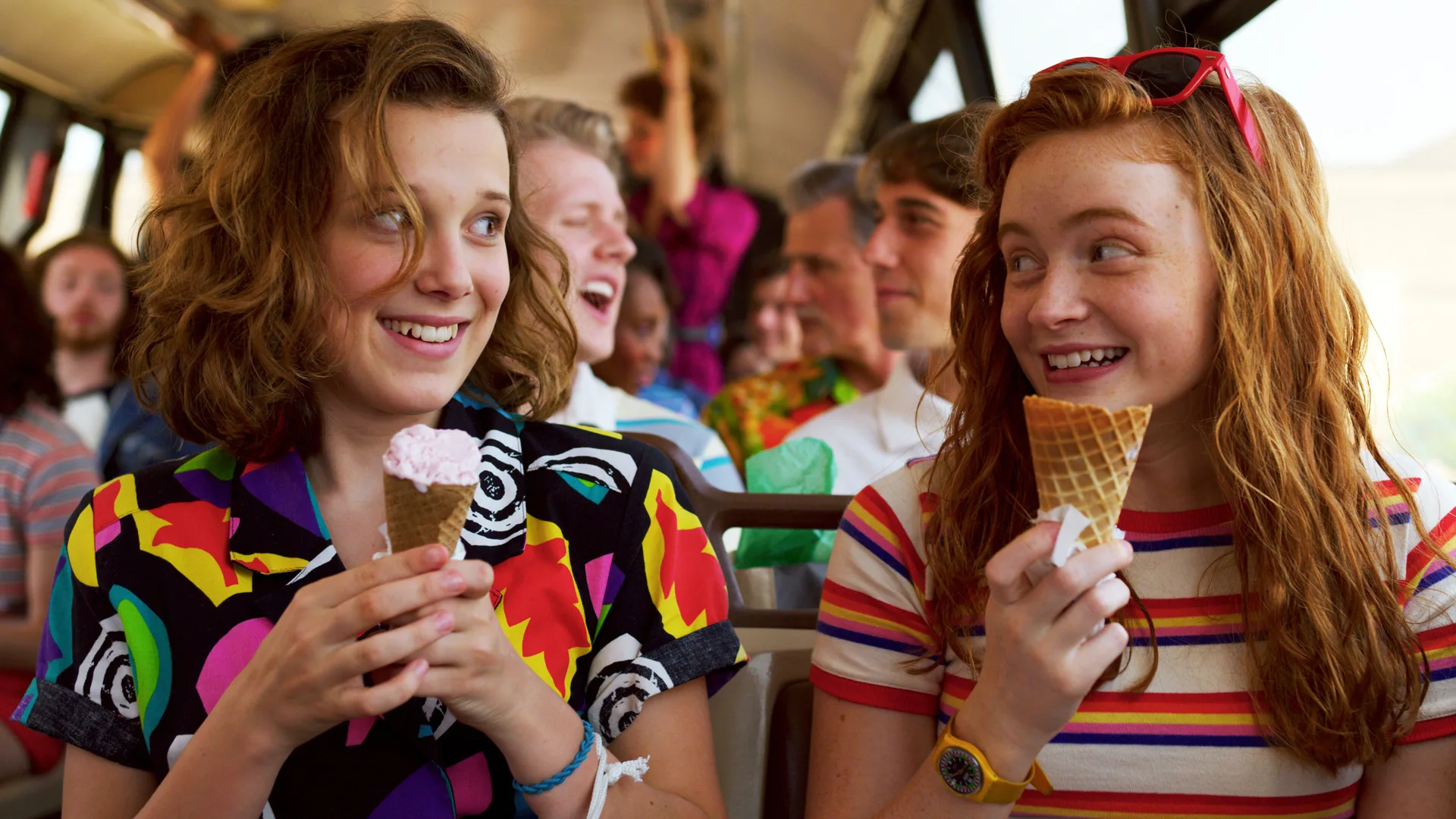 A photo of the characters Eleven and Max from Stranger Things both smiling at eachother on a bus holding icecreams