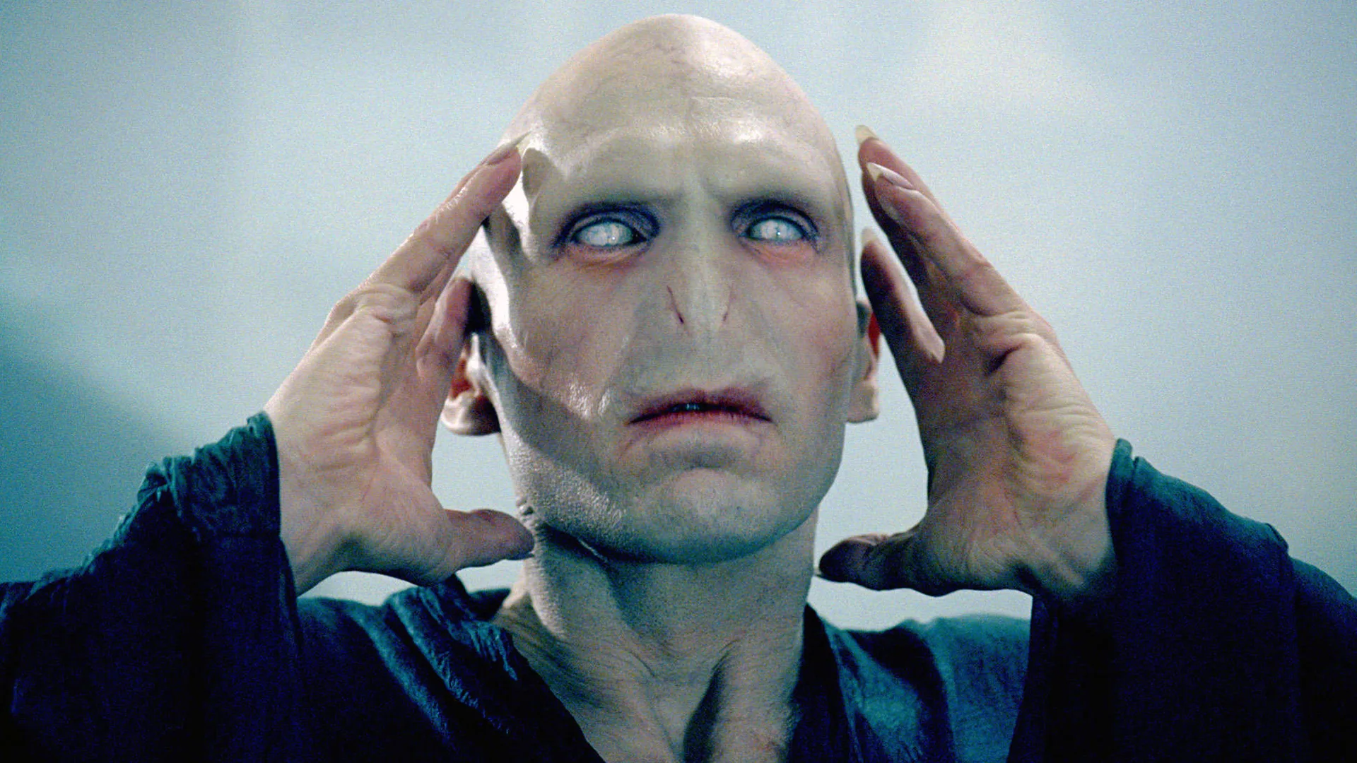 A still from Harry Potter showing Voldemort holding his head with white eyes against a smoky background