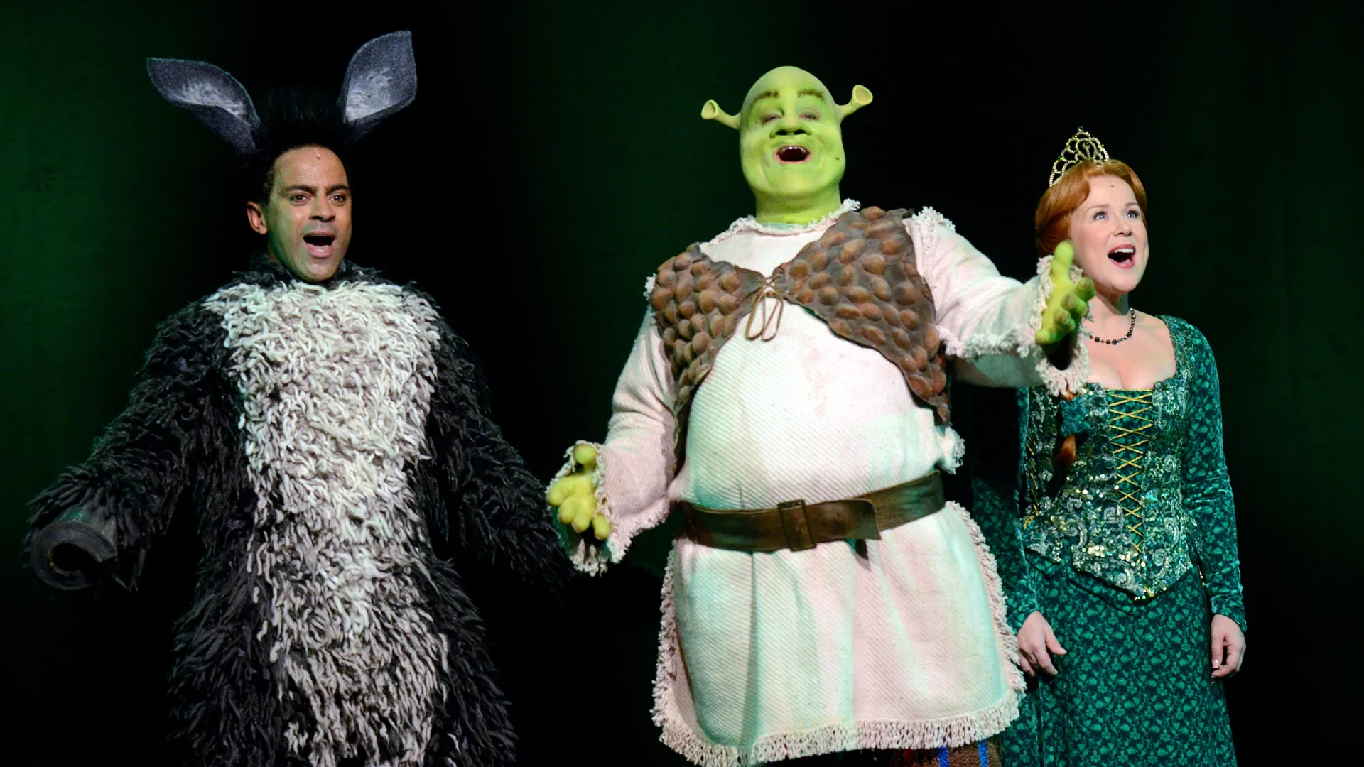 A photo of Shrek the Musical showing Donkey, Shrek and Fiona singing on stage