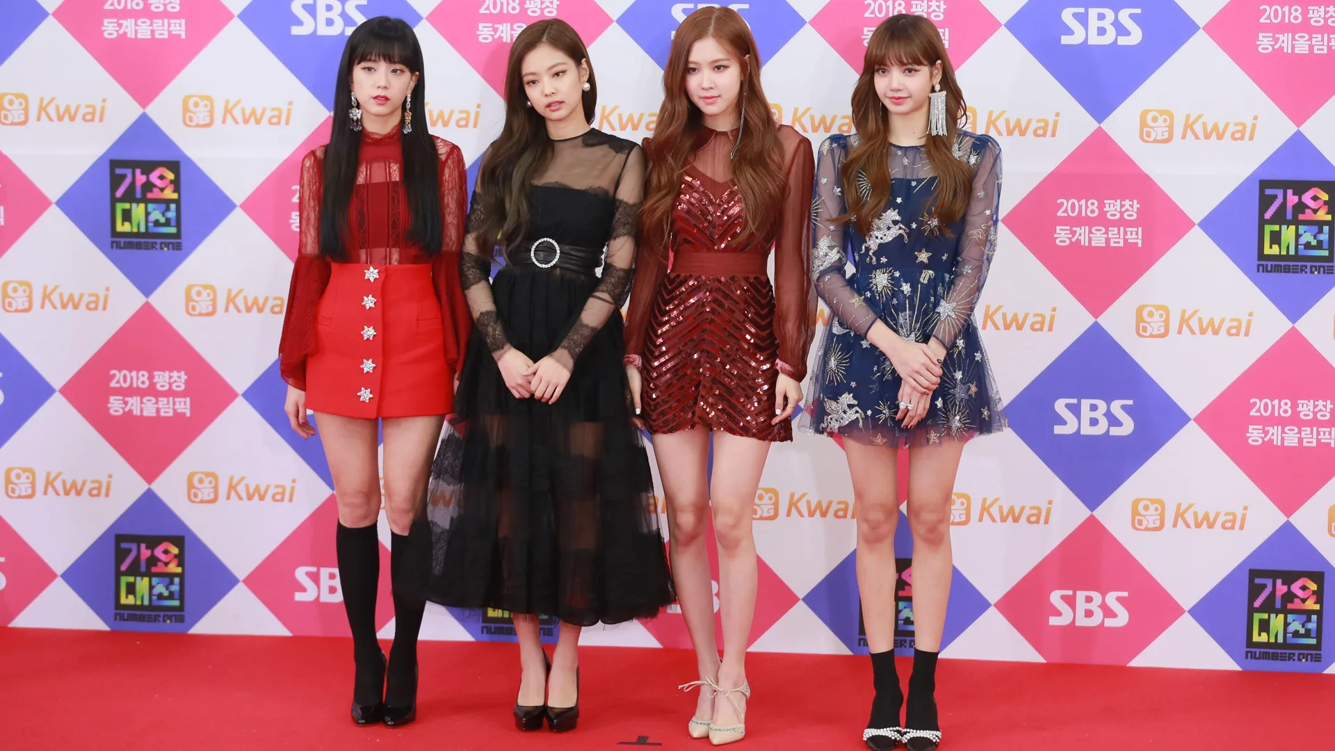 A photo of the k-pop band Blackpink stood on the red carpet - all four members are wearing different outfits with their hands crossed