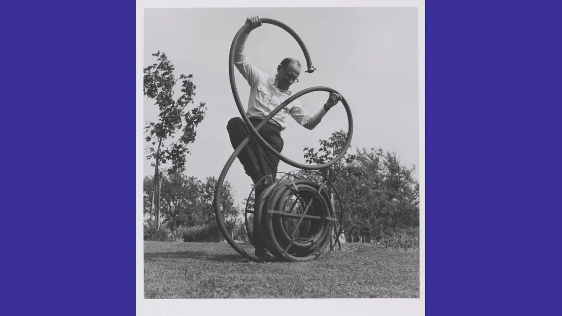 A black and white photograph of a man fighting with a garden hose in an English country garden