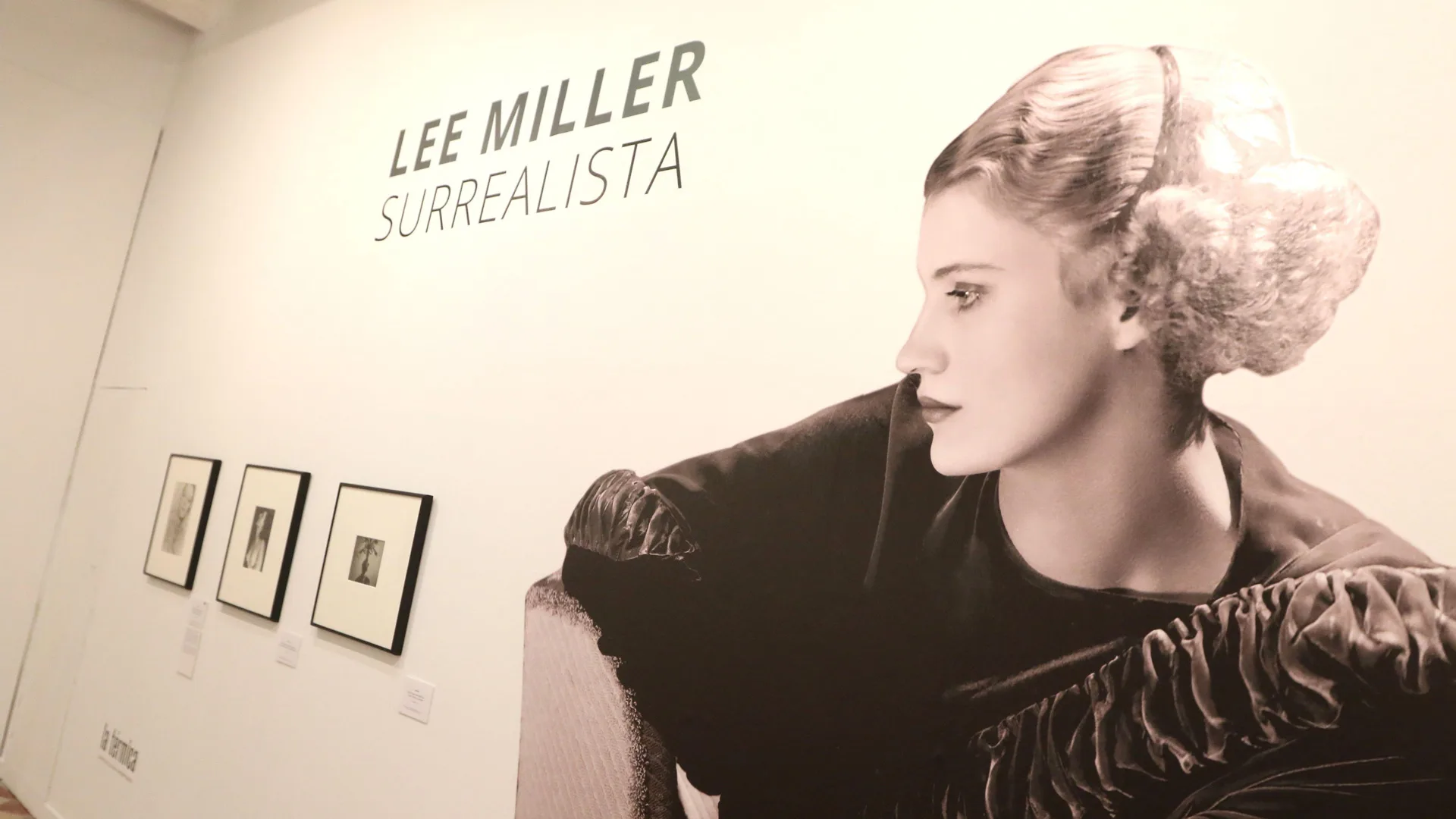 A sepia image of a Lee Miller exhibition with the model herself sat side on looking down and the text LEE MILLER SURREALISTA