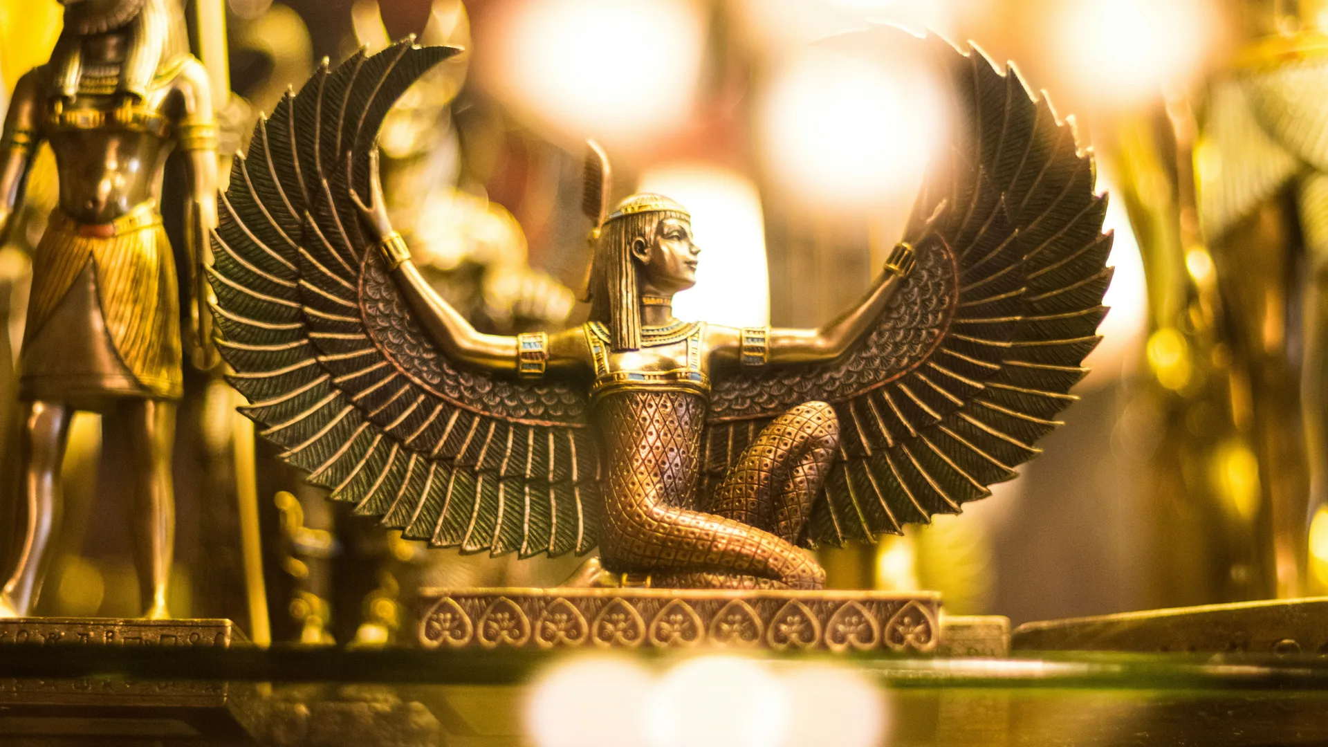 A photo of a gold statue of an Ancient Egyptian Goddess with large wings spread out surrounded by gold and bright light.