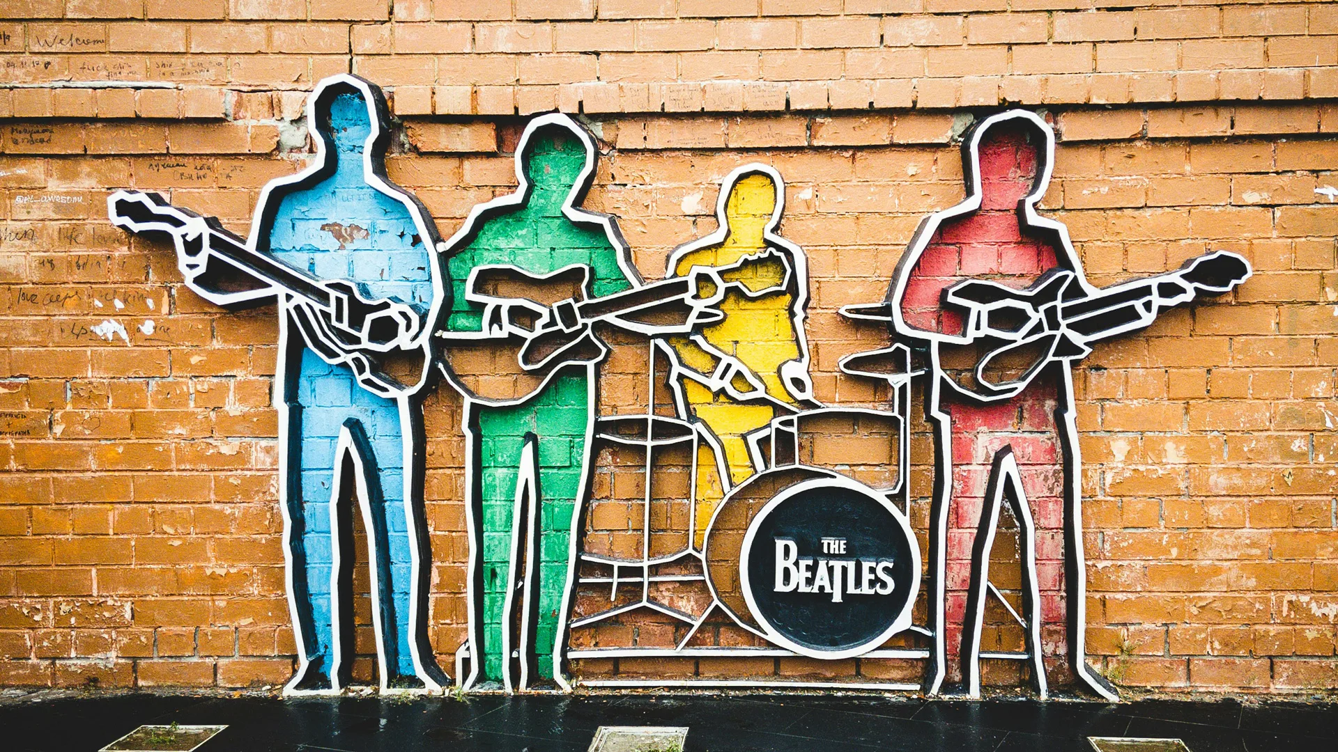 A photo of a sculpture against a wall in blue green yellow and red of outlines of the four members of the band the beatles