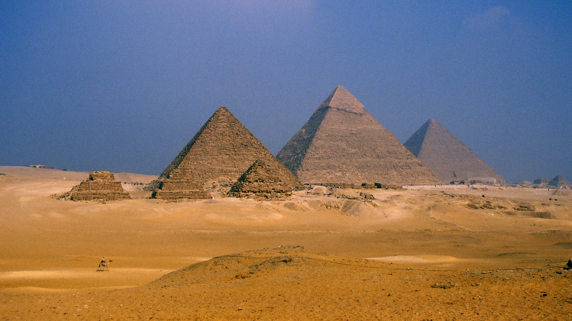 A photo of the pyramids of Giza in the desert with blue sky.