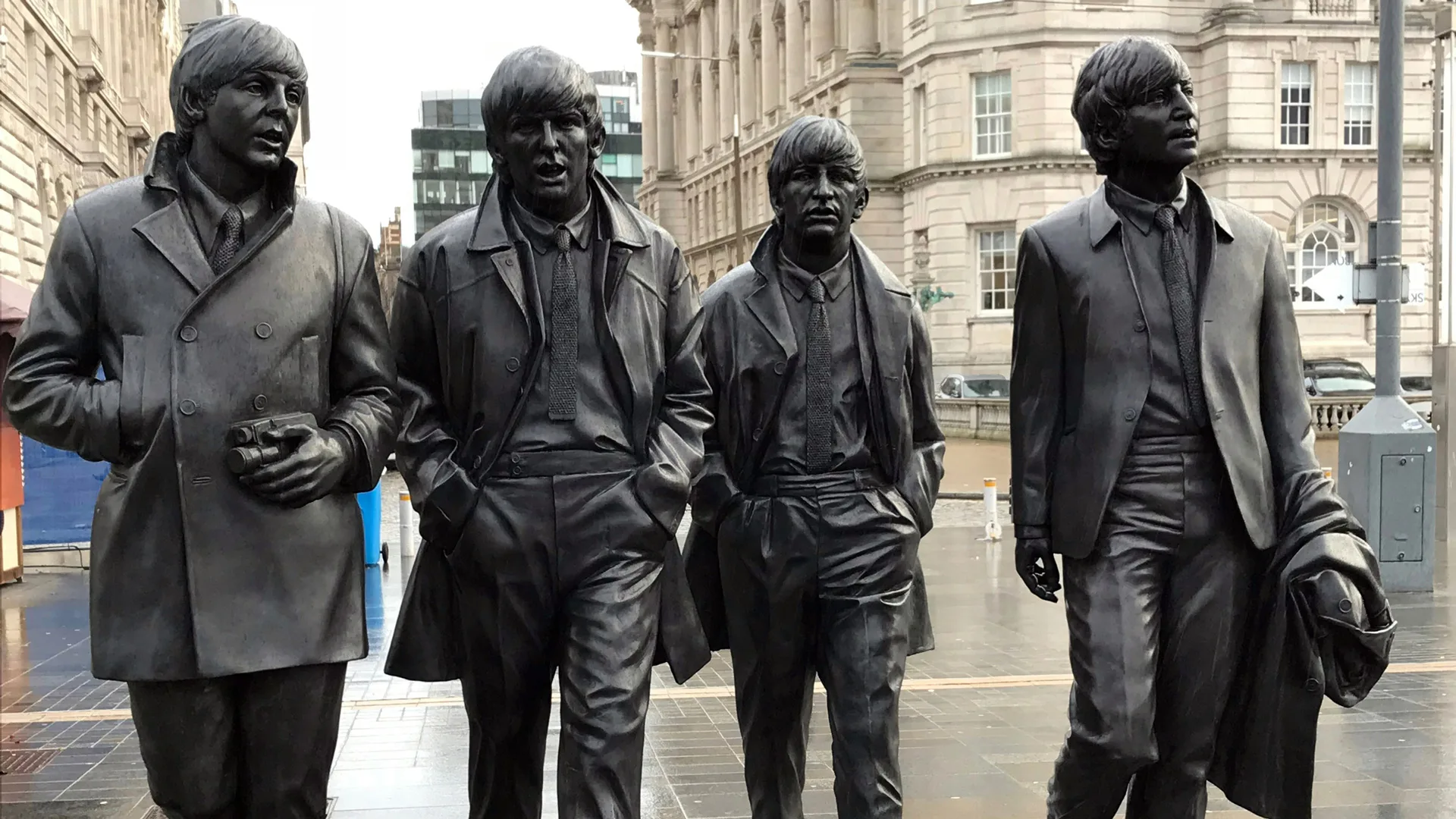 A photo of the Beatles statues in Liverpool in mid-walk against a grey cityscape