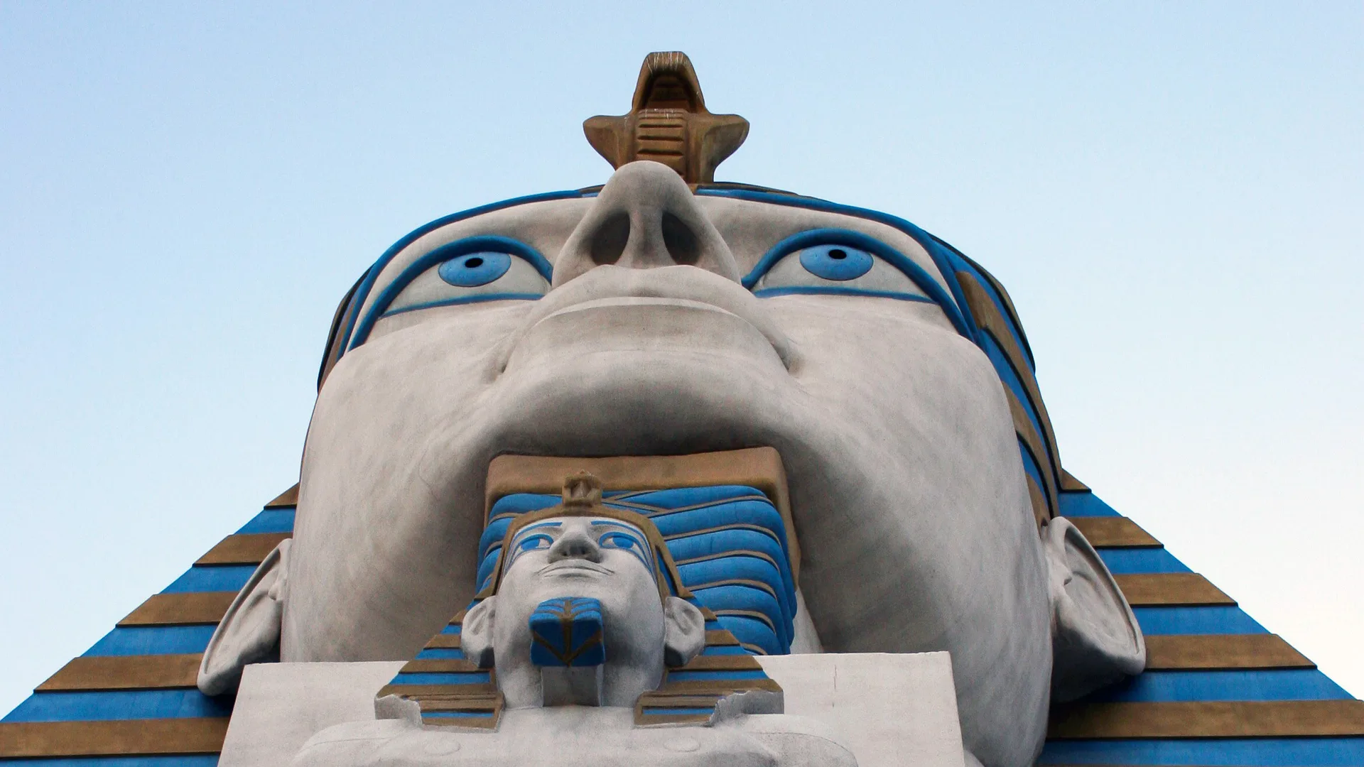 A photo of a Pharoah statue from the perspective of standing underneath it. There is a small head and a much bigger head with a blue sky.