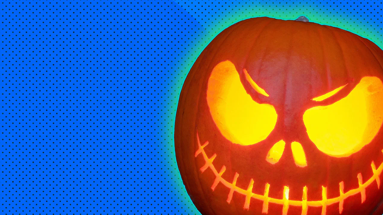 A photo of a Halloween pumpkin with a smiling skull face carved into it with a green halo against a blue dotted background.