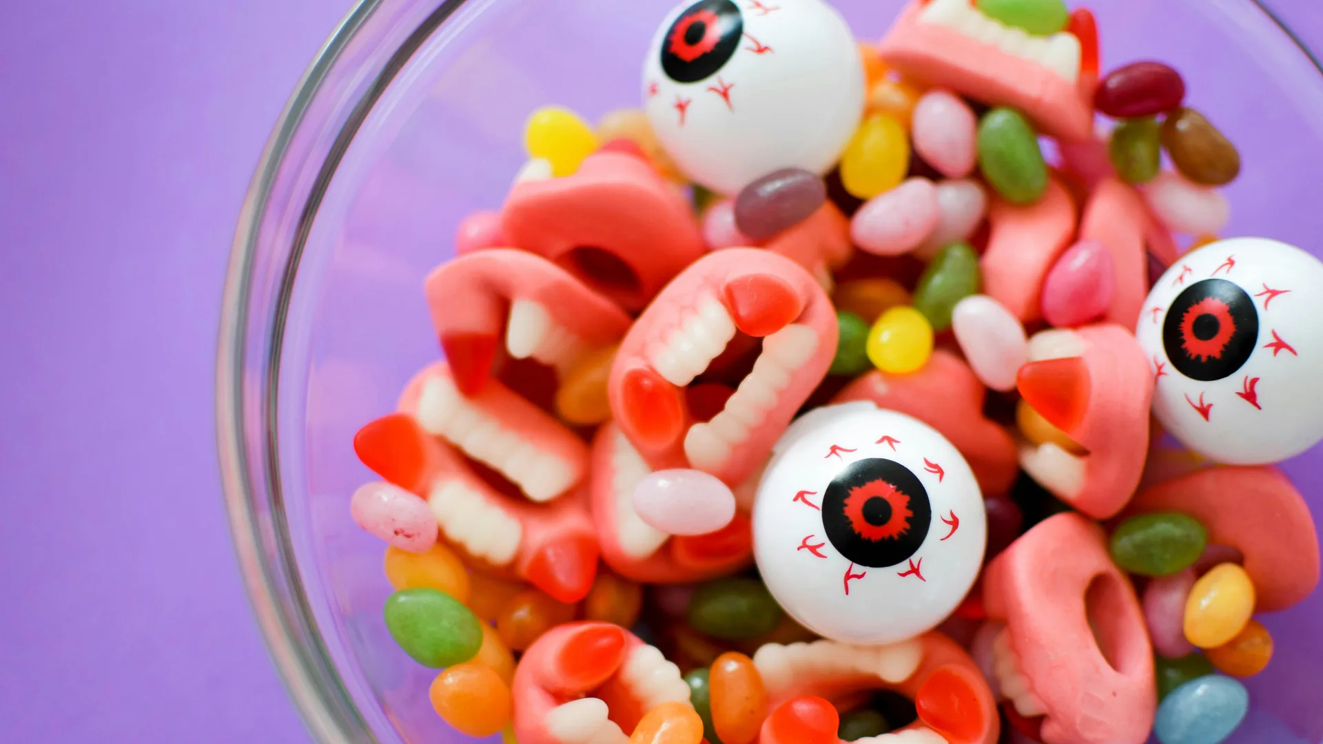 A photo of a bowl of Halloween sweets made up of teeth, eyeballs and jelly beans sitting on a purple table.