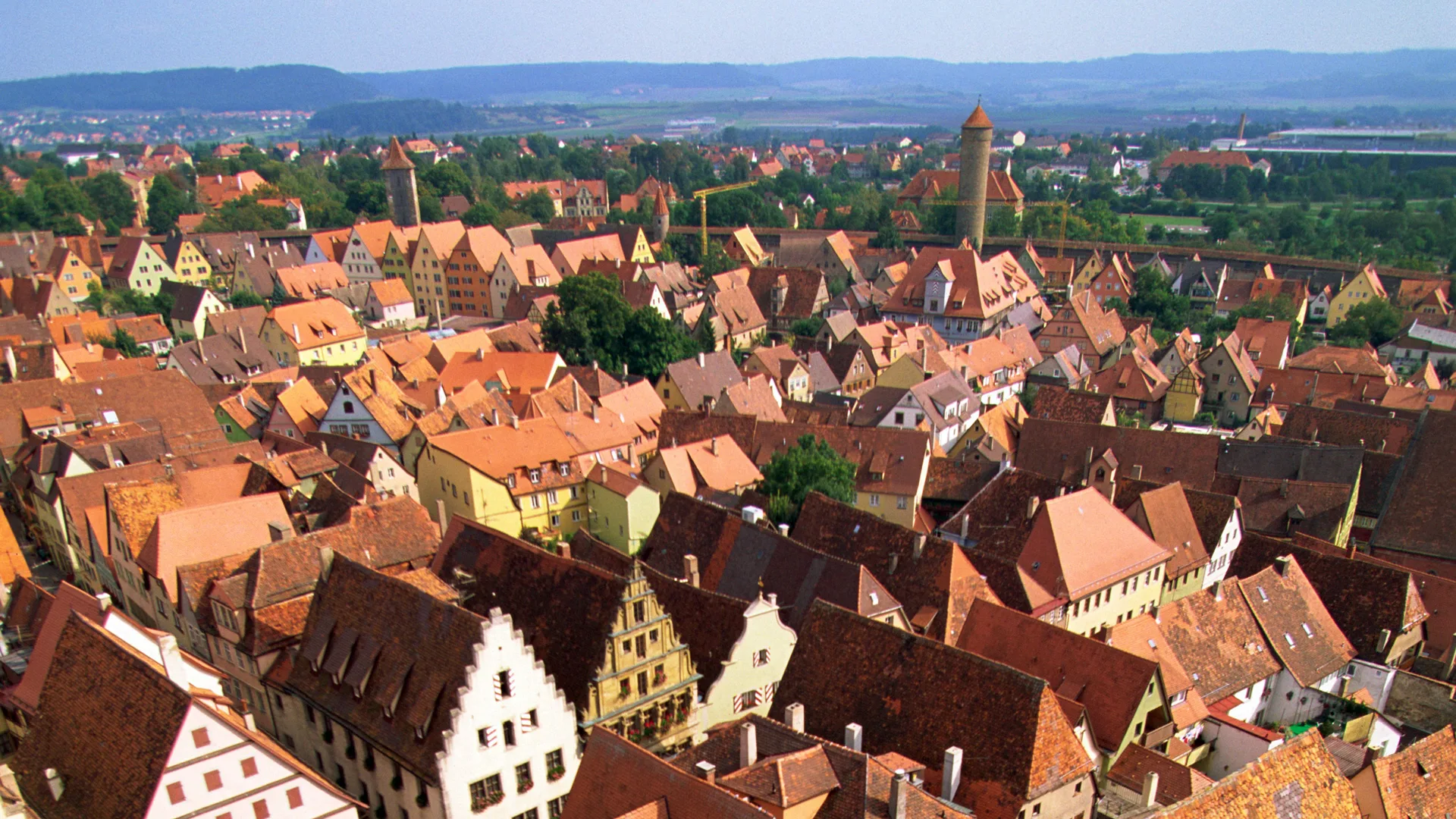 A photo of a town with red tiled roofs from above with the horizon line far in the background