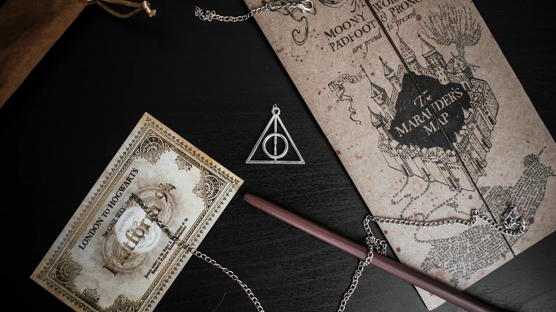 A photo of a Harry Potter ticket for the train, a wand, a necklace with the Deathly Hallow symbol and a Maurader's Map.