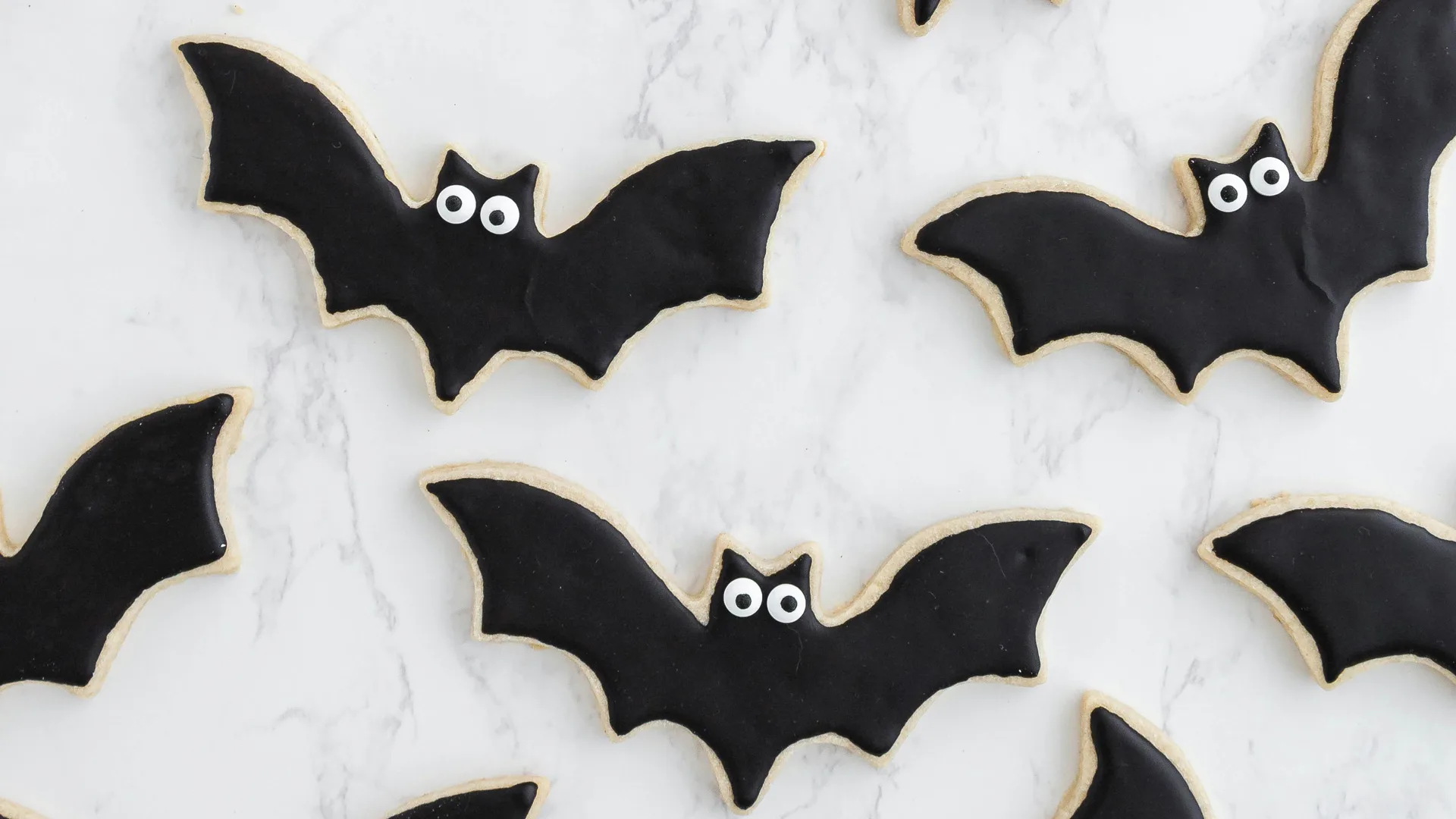 A photo of halloween bat bicuits with little eyes laid out on a marble top surface.