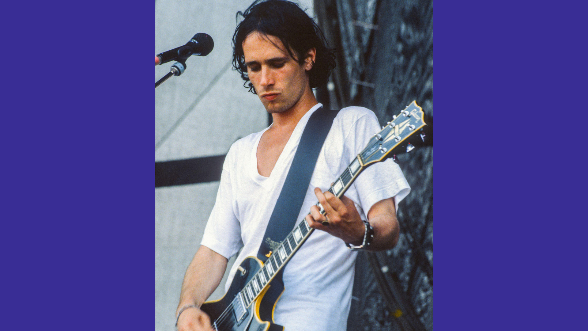 A photo of Jeff Buckley playing guitar on stage looking down with a microphone in shot.