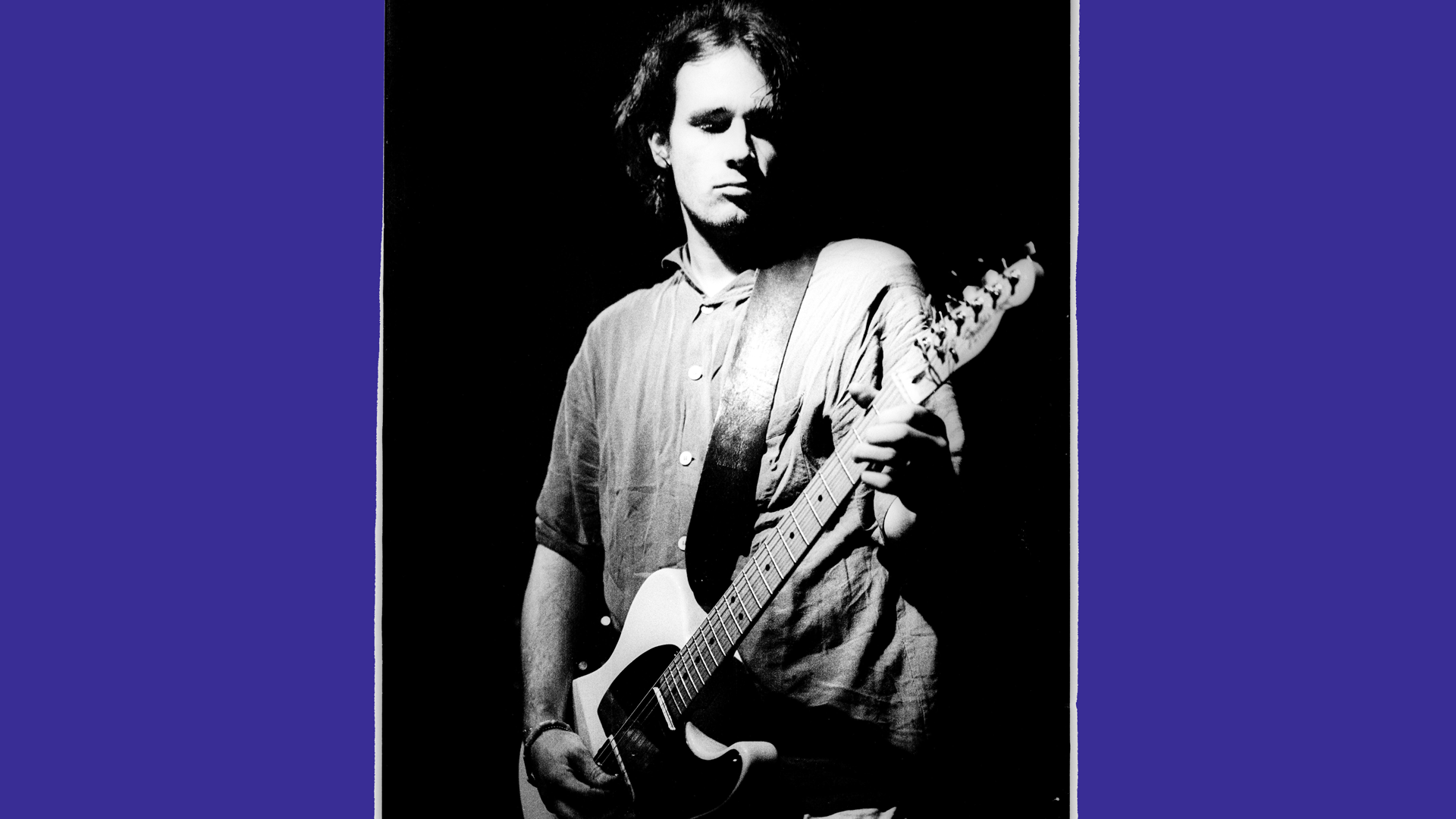 A black and white photo of Jeff Buckley holding a guitar against a black background with purple borders.