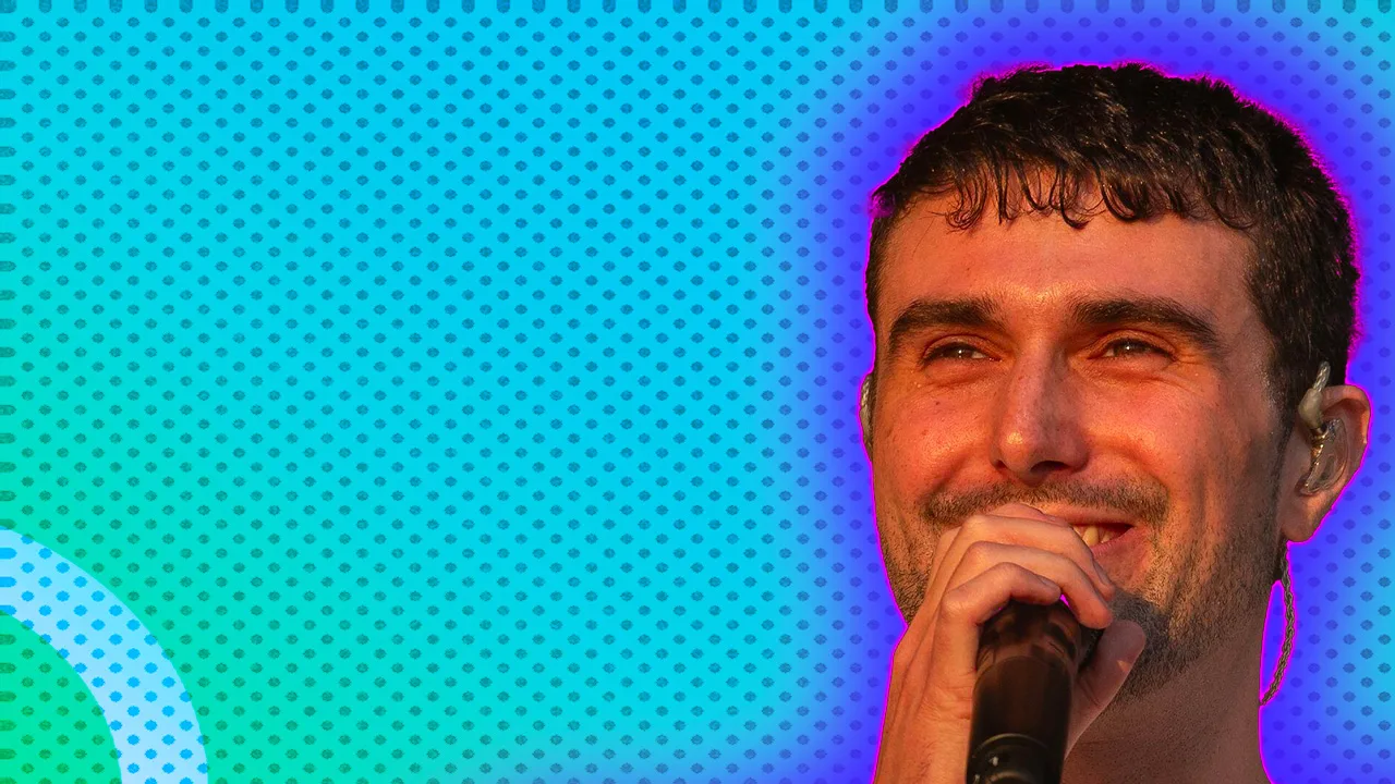 A photo of the musician Fred Again smiling into a mic against a blue background with a purple halo.