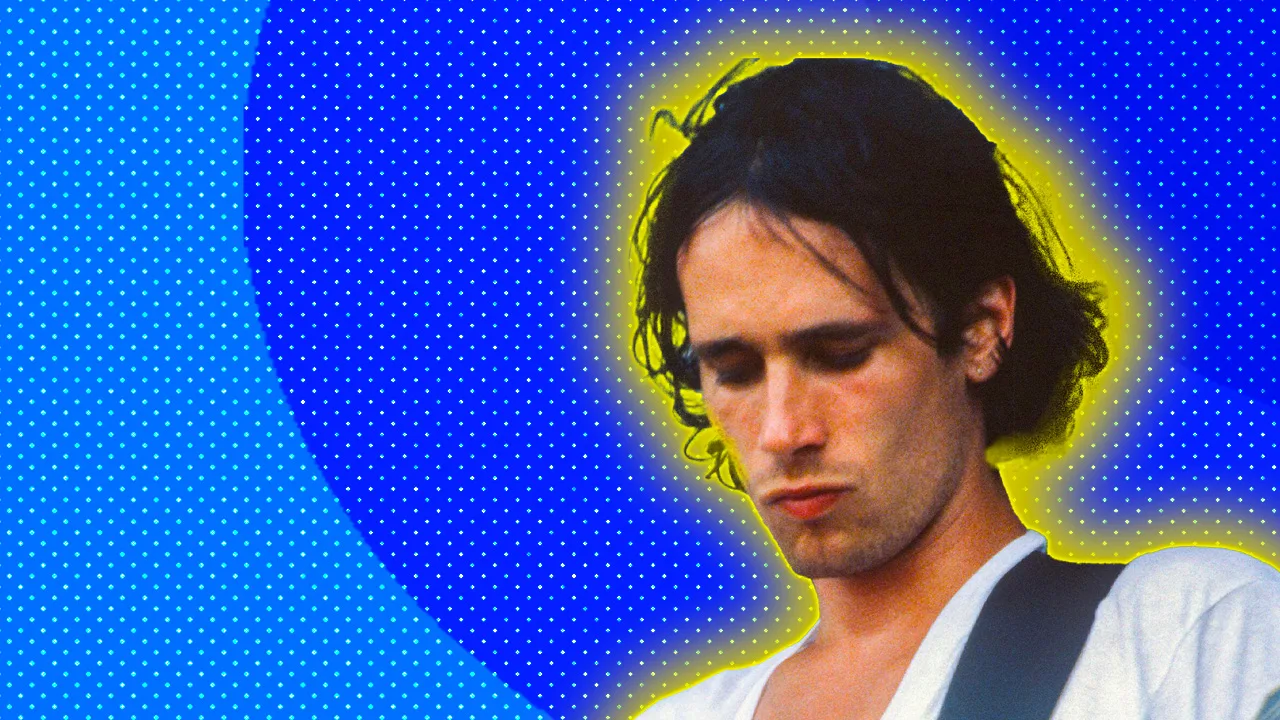 A photo of Jeff Buckley wearing a white tshirt looking down against a blue dotted background with a yellow halo.