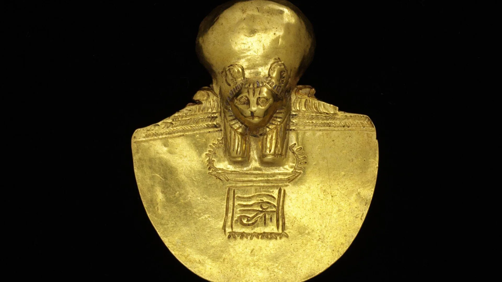 A photo of a gold bust collar of the lion-headed Ancient Egyptian goddess Sekhmet against a black background.