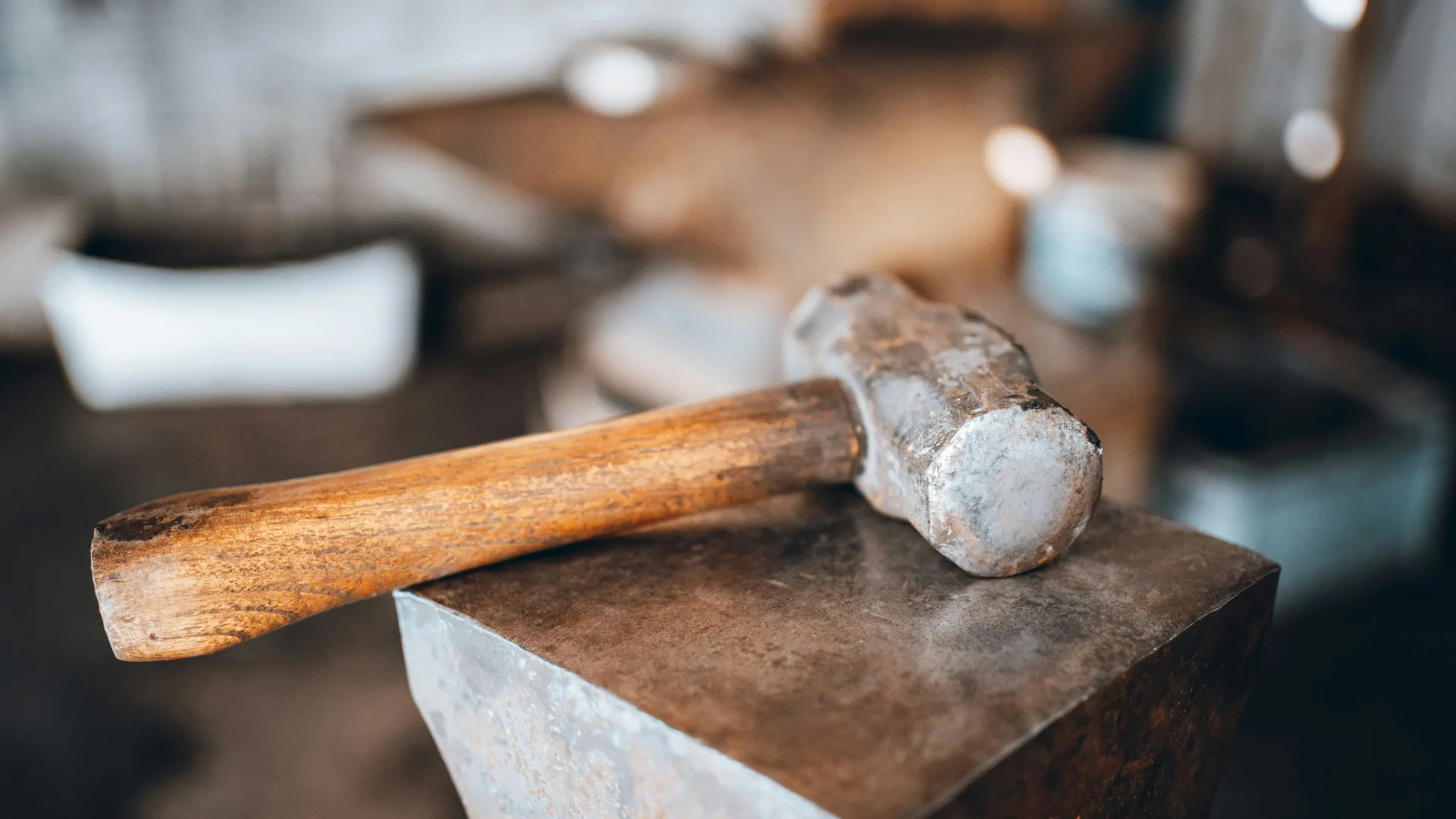 A photo of a hammer laying on a anvil against a workshop background.