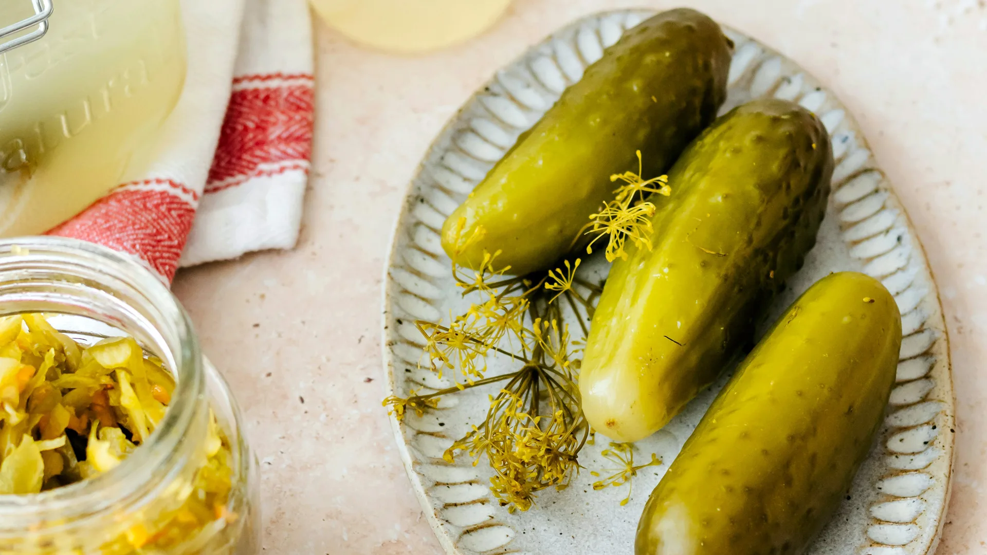 A photo of pickles on a plate next to a jar of shredded pickle with a red and white napkin next to them.