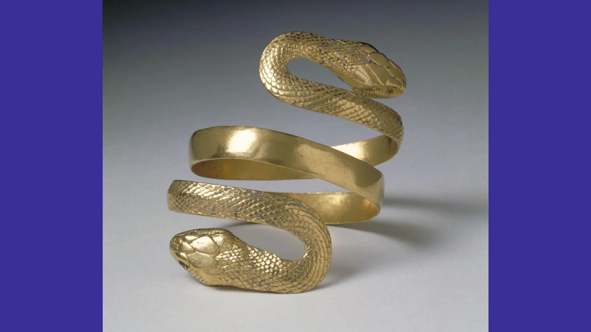 A photo of a gold snake armlet against a grey background,