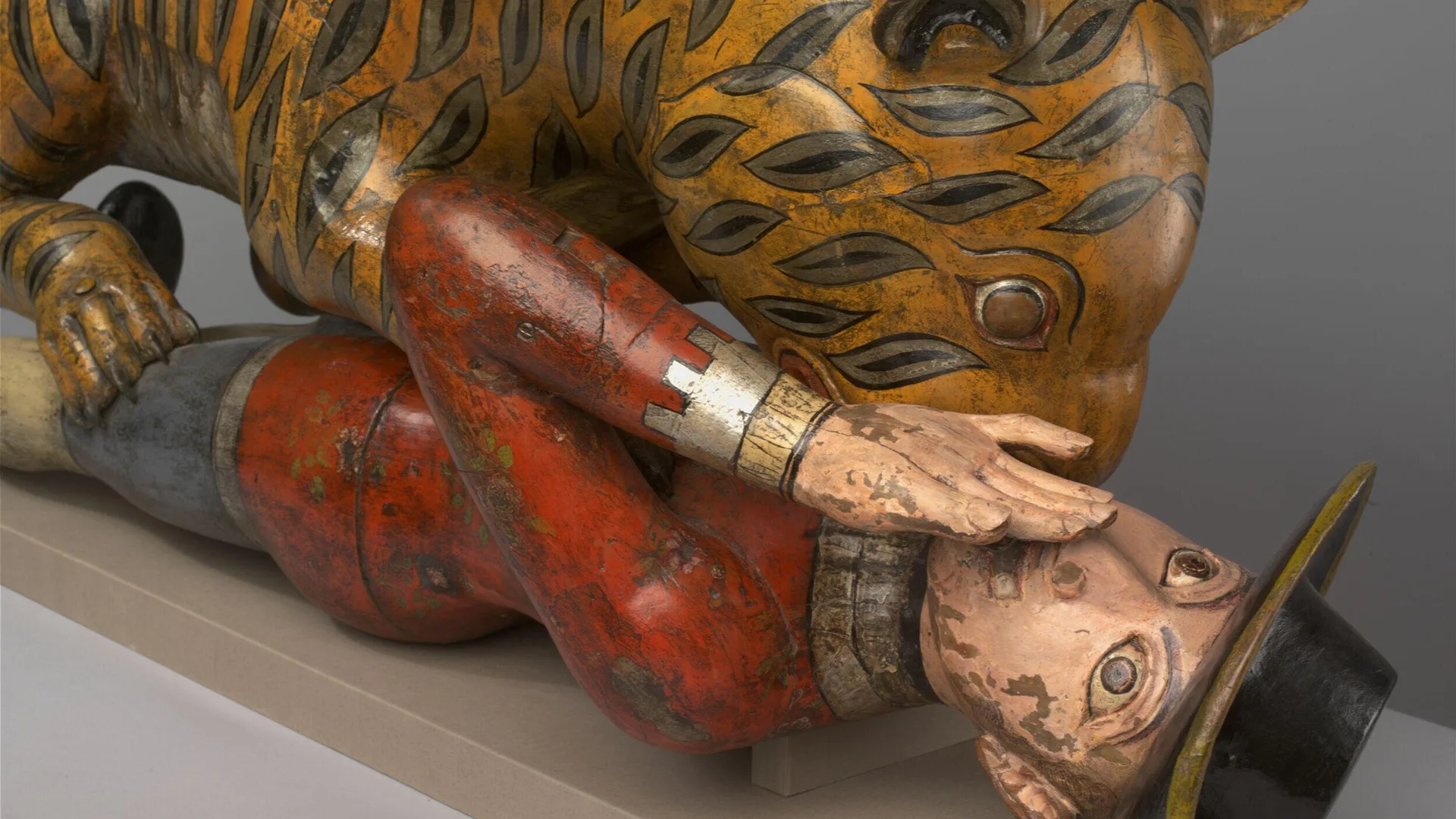 A close up of the V&A object Tippoo's Tiger showing the soldier screaming with a hand over his face. He is wearing a red jacket and black hat.