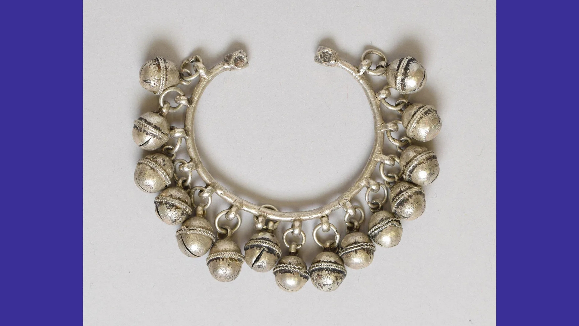 A photo of a silver bangle with little bells against a grey background.