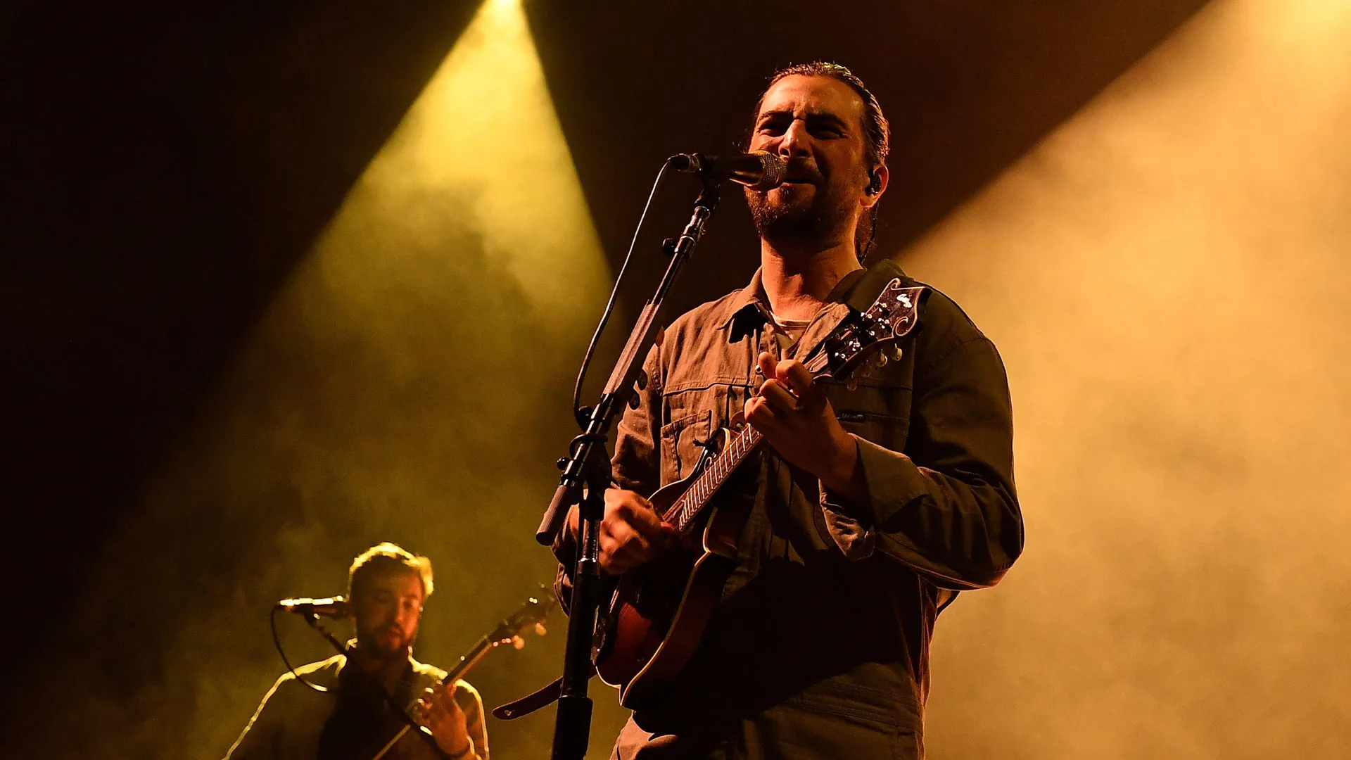 A photo of Noah Kahan singing on stage with orange light on him.