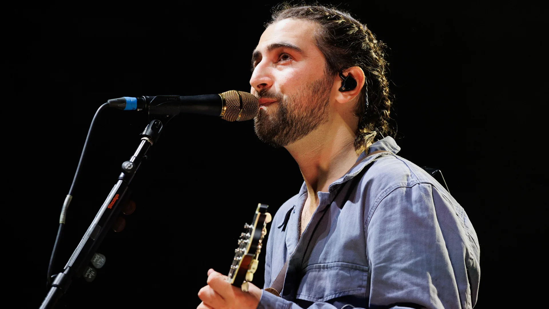 A photo of Noah Kahan singing into a mic with a black background.