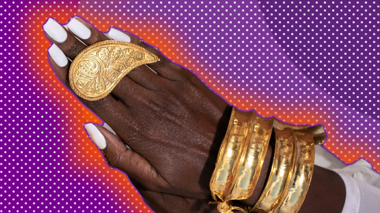 A photo of a hand with white nails and gold jewellery adorning it against a purple dotted background with an orange halo.