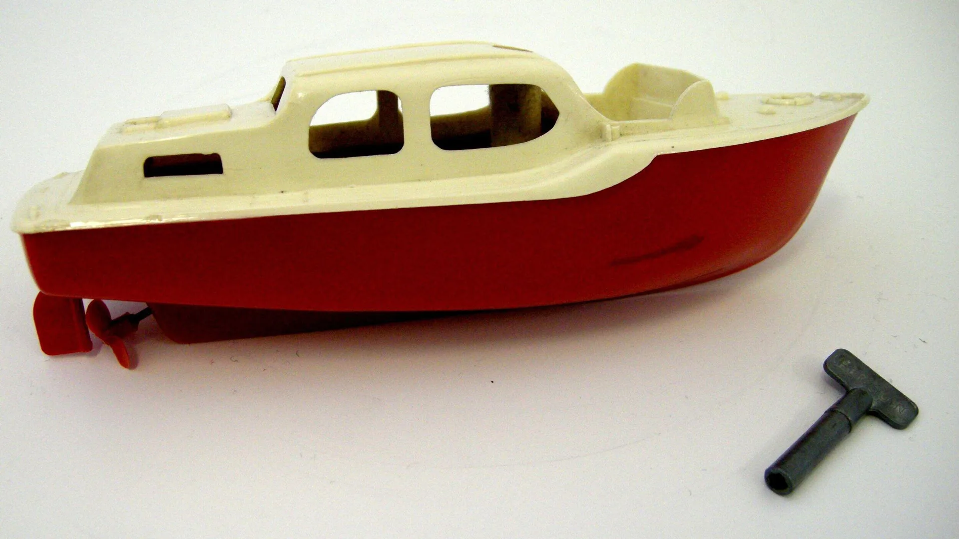 A photo of a red and white toy boat with a little anchor next to it on a white surface.