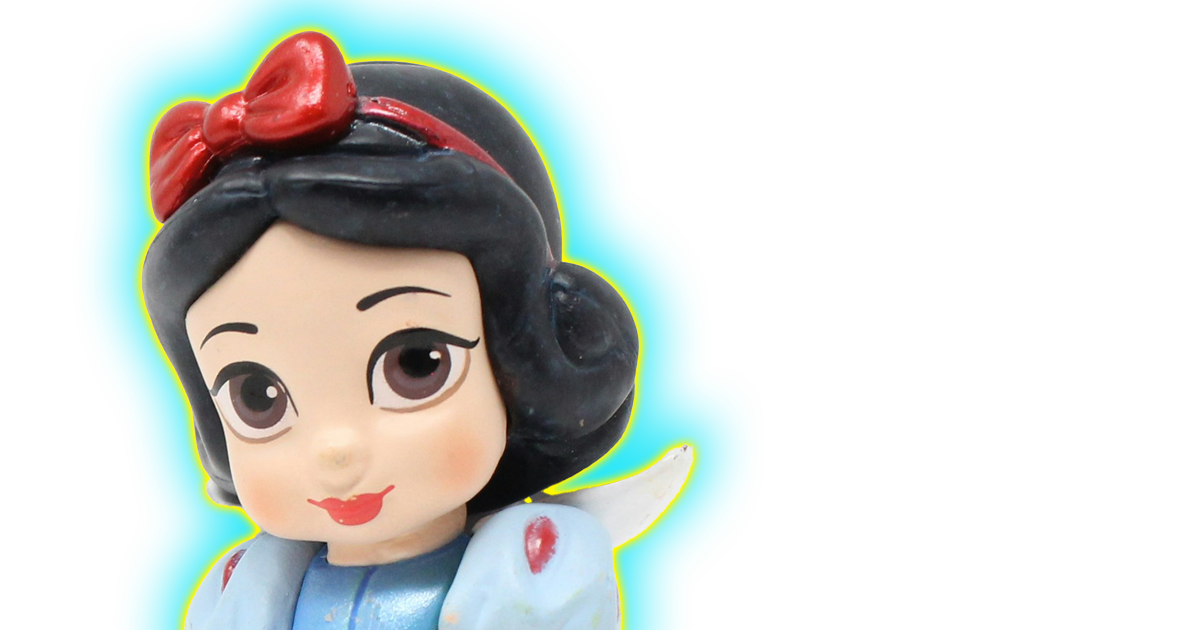 A photo of a Snow White figurine smiling at the viewer with her signature red bow and blue and yellow dress. She has a yellow and blue halo around her.