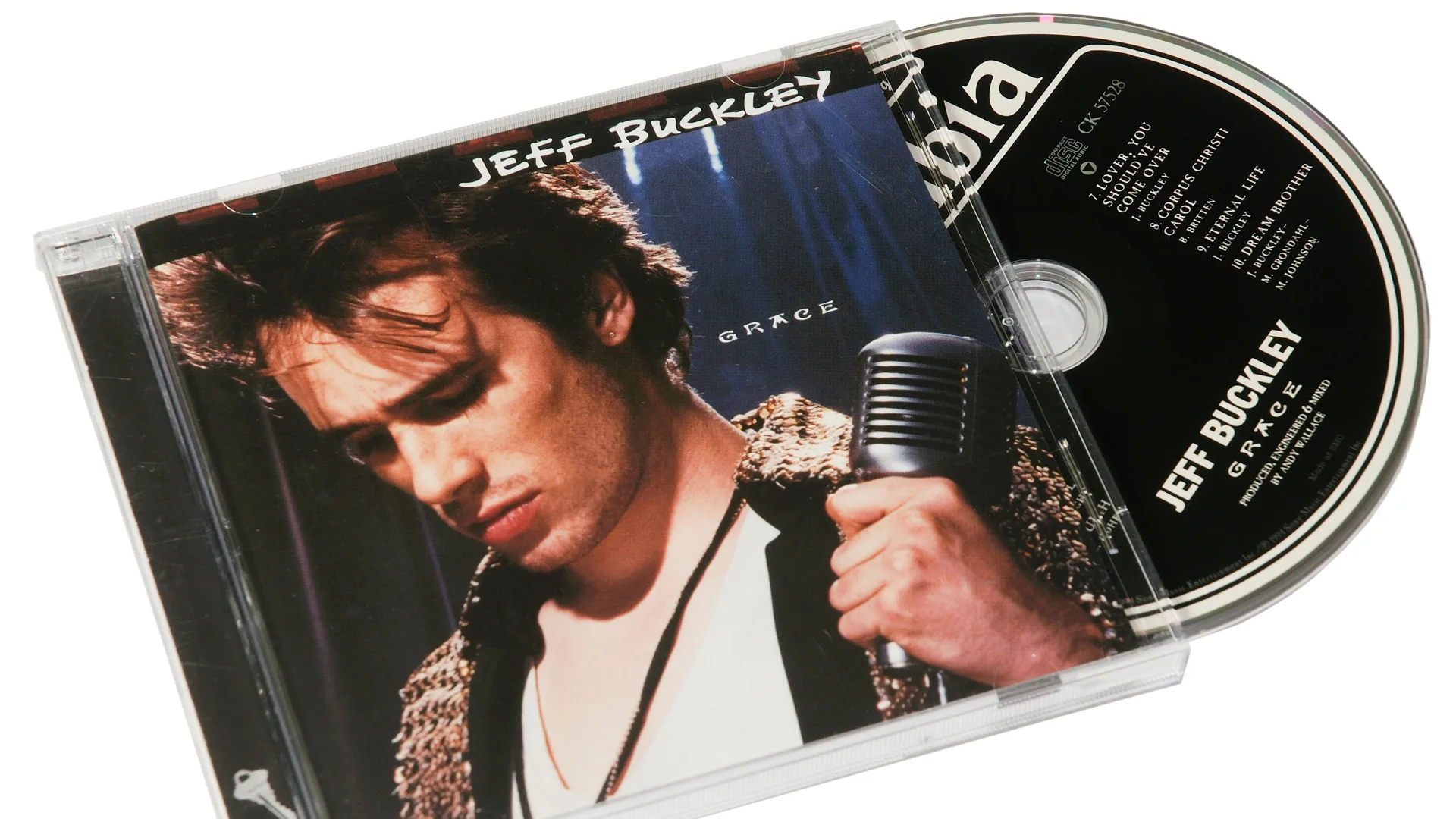 A photo of Jeff Buckley's album Grace in CD format showing the front cover with Jeff holding a microphone, looking down against a blue background with the words JEFF BUCKLEY and GRACE around him. The CD is partially exposed from the case in black and white text. The CD is on a white background.