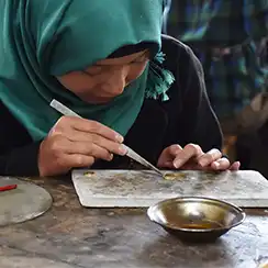 A jewellery artisan wearing a green veil works on a piece of jewellery.