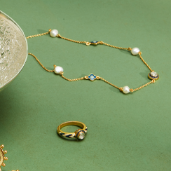 A thin gold chain necklace and a ring featuring a polki diamond are propped on a green top.