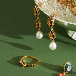 A gold ring and a pair of drop earrings on a green background.